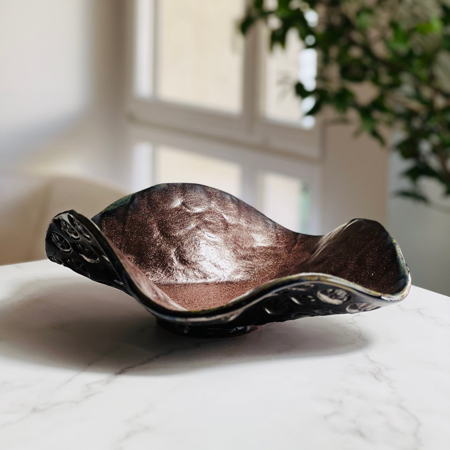 Handmade medium decoraåtive rose gold ceramic bowl displayed on a marble table with a living room background.