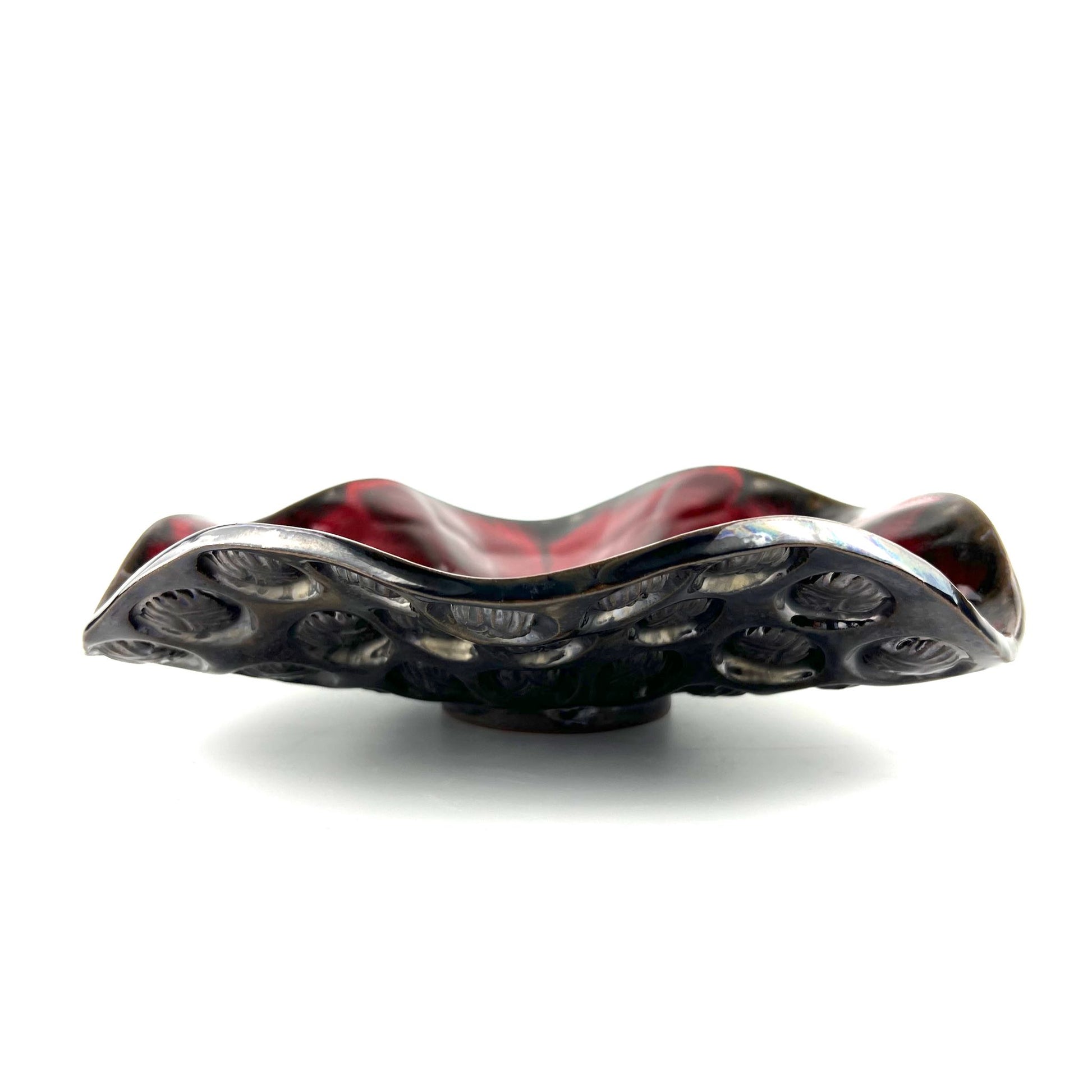 Side view of a handmade medium-sized decorative ceramic bowl featuring a glossy rich red interior and beetle texture design.