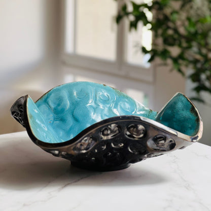 Handmade medium-sized decorative turquoise ceramic bowl with hand and ant texture displayed on a marble table with a living room background.