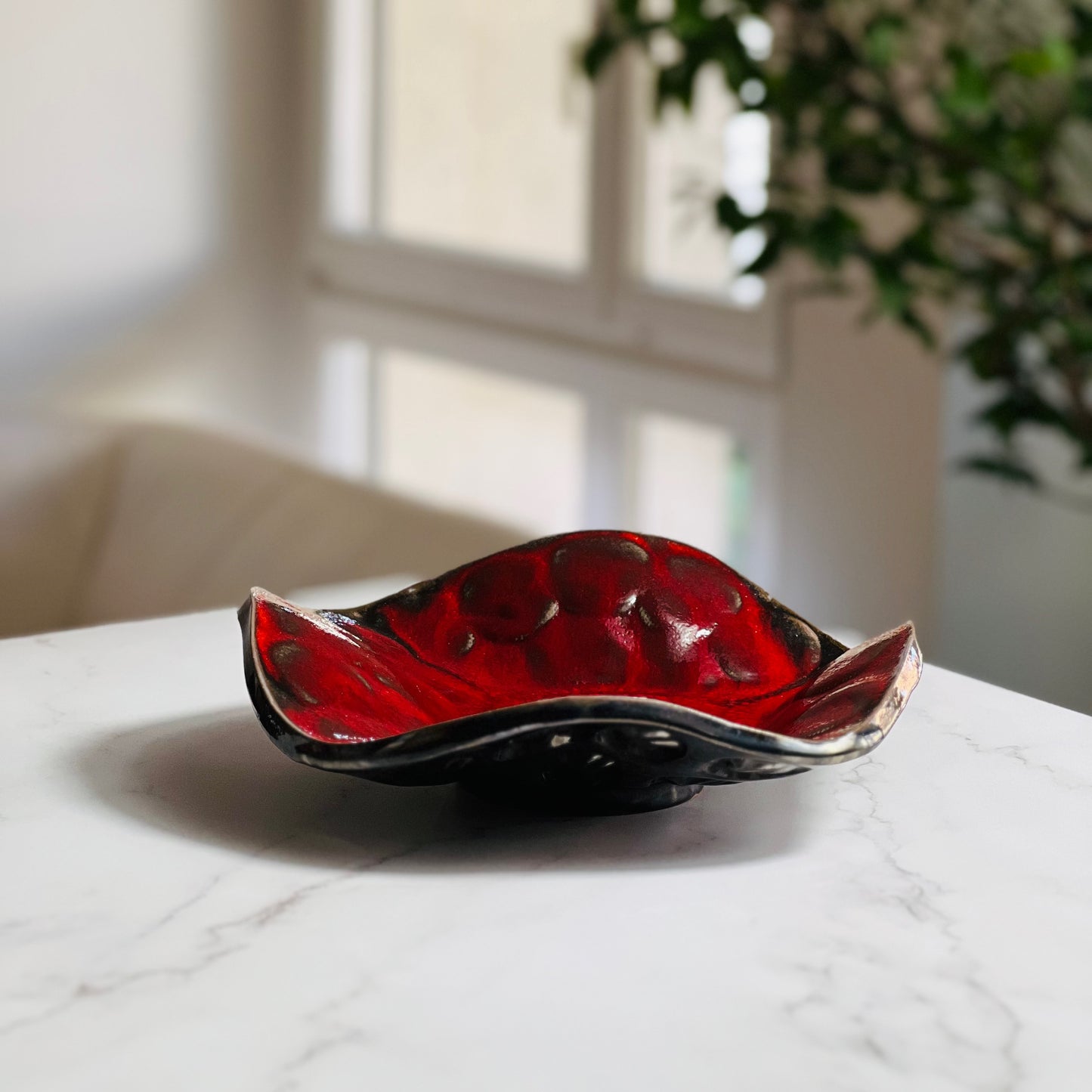 Handmade small-sized decorative rich red ceramic bowl with tree texture displayed on a marble table with a living room background.