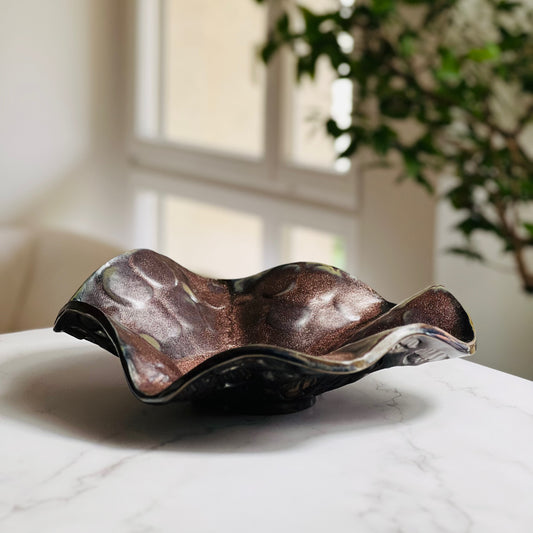 Handmade small decorative rose gold ceramic bowl displayed on a marble table with a living room background.